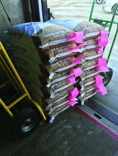 The yellow feed cart tires in the trailer/box do not cross the line of separation. Product positioned over the line of separation is removed with the green cart and stored in a compartment outside of the truck. Disposable foot protection is put on each time before crossing the line of separation moving from liftgate into truck box. (Courtesy United Animal Health)