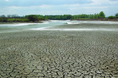 a shallow river from drought with cracked earth in the foreground against a blue sky on a hot sunny day
