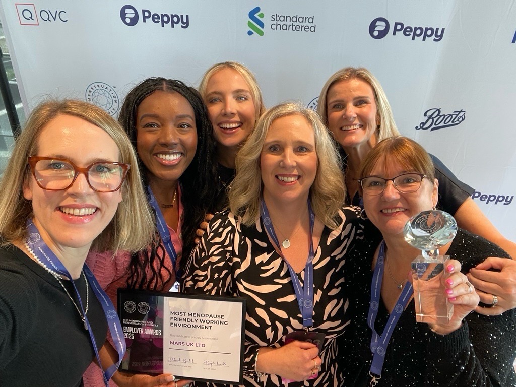 Seven women smiling together at corporate event, holding award certificate