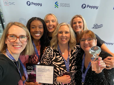 Seven women smiling together at corporate event, holding award certificate