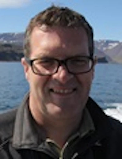 Smiling man with glasses outdoors near water and rocky landscape