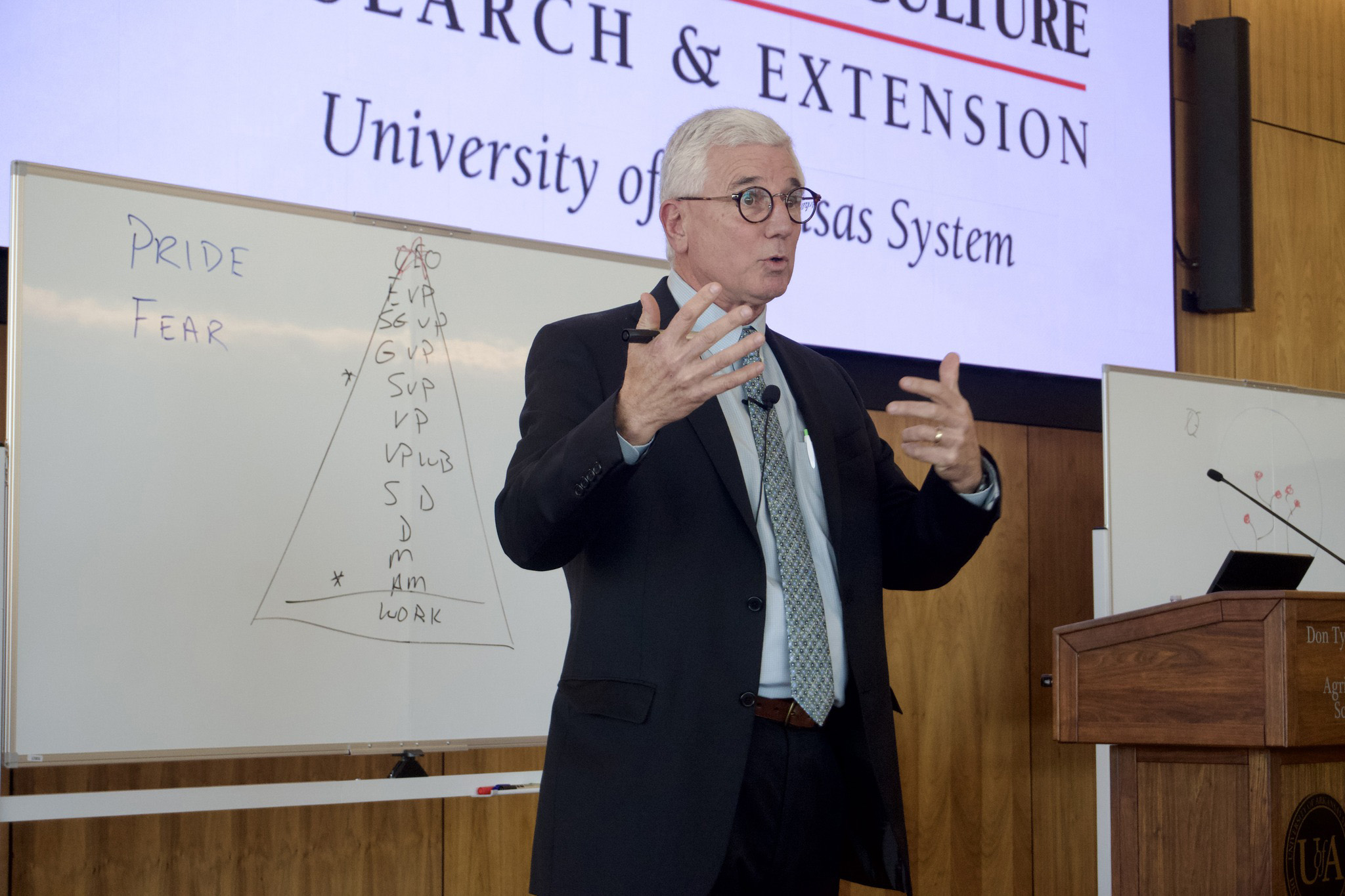 Speaker presenting research lecture with whiteboard diagram at University of Texas System
