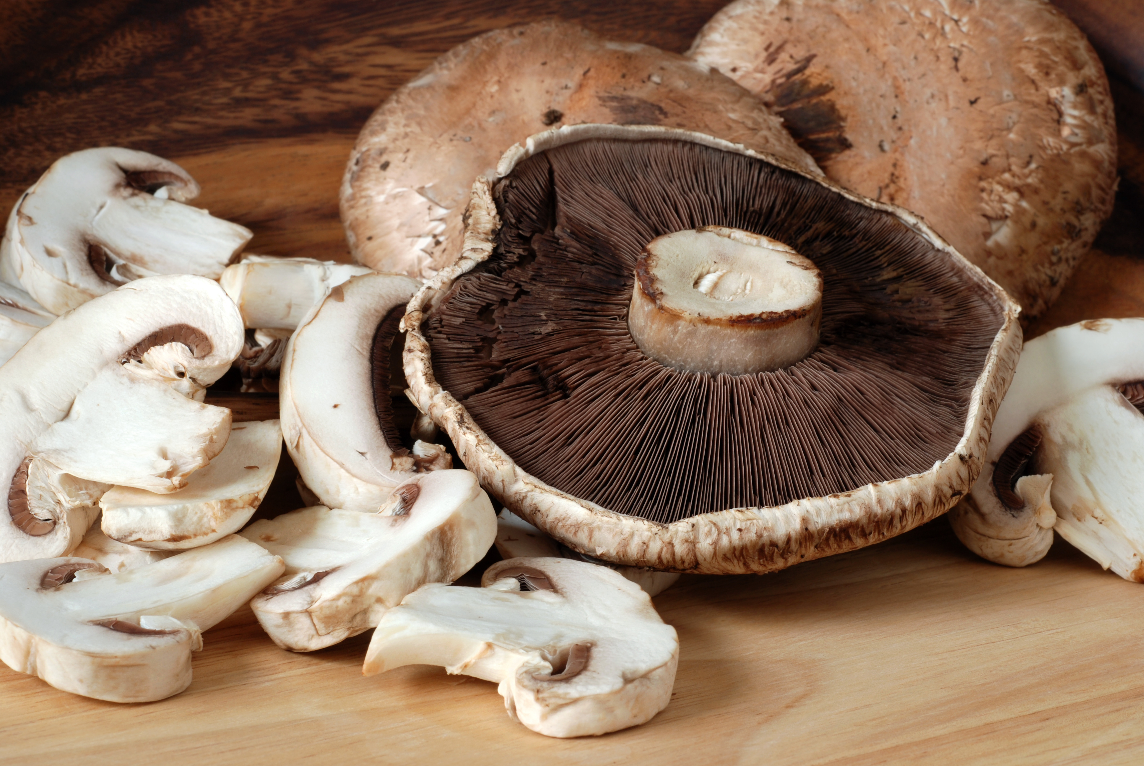 Fresh portobello and white button mushrooms sliced on wooden cutting board