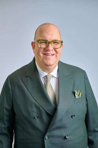 Smiling professional in green suit and glasses against neutral background