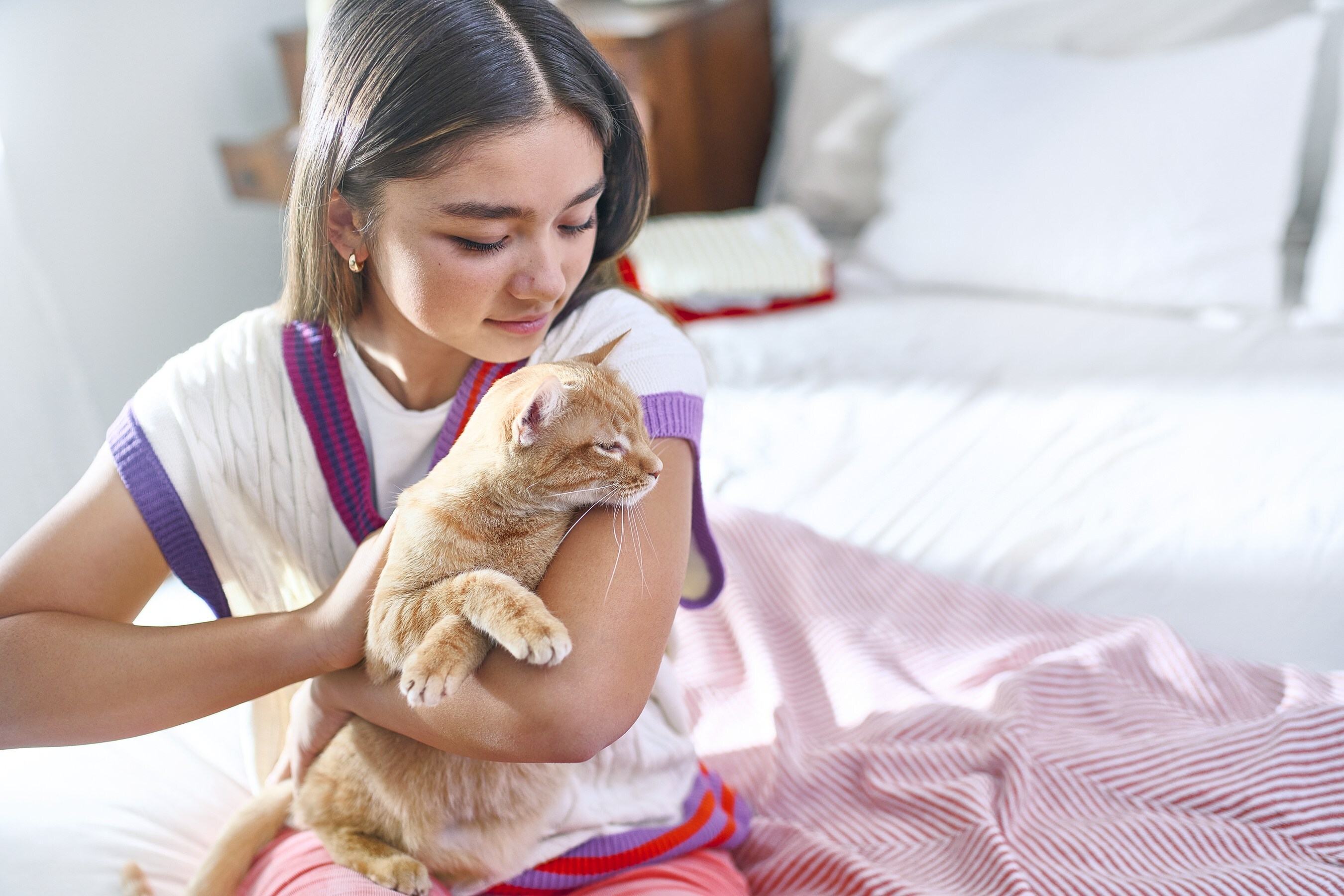 Young person gently holding an orange tabby cat in a cozy bedroom
