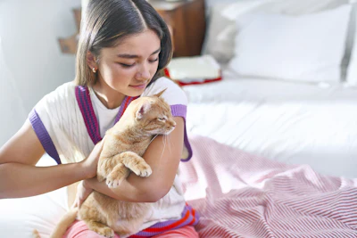 Young person gently holding an orange tabby cat in a cozy bedroom