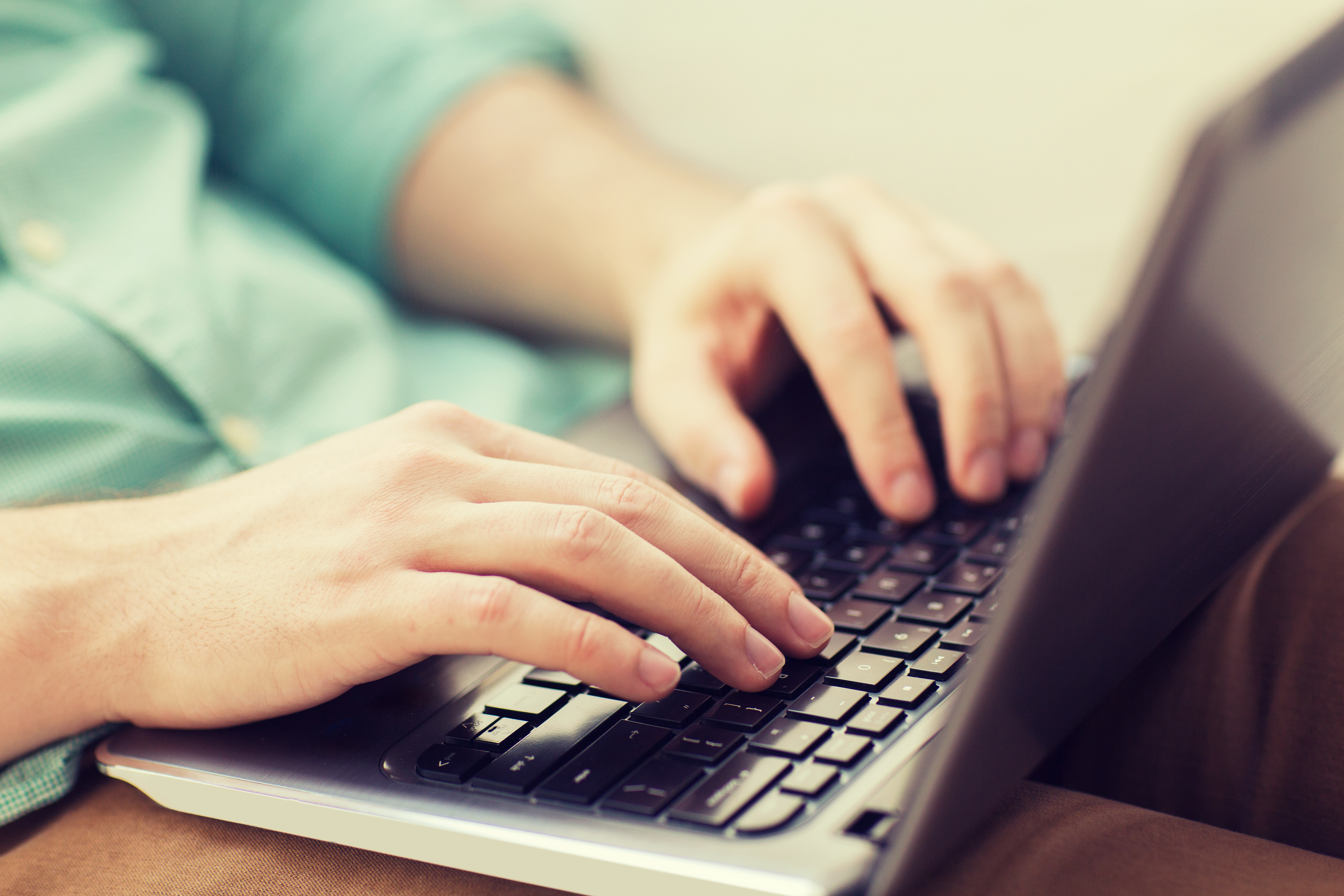 Hands typing on laptop keyboard, wearing light blue shirt sleeve