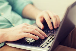 Hands typing on laptop keyboard, wearing light blue shirt sleeve