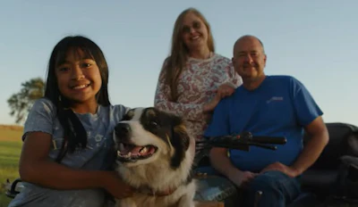 Smiling family with young girl, dog, and adults outdoors at sunset