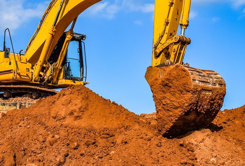 Yellow Caterpillar excavator digging into reddish-brown earth against blue sky