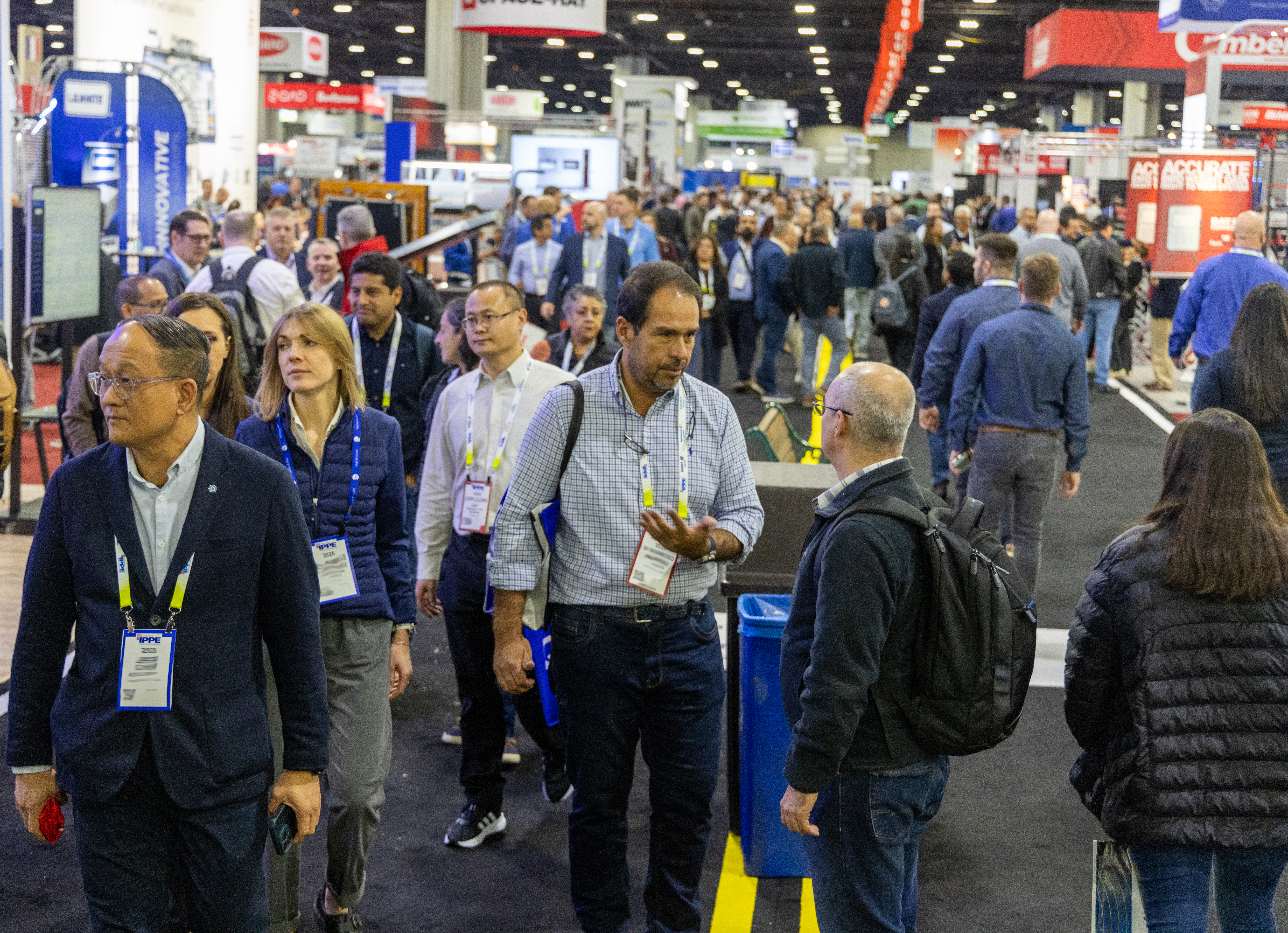 Crowded trade show floor with professionals networking and walking between exhibition booths