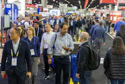Crowded trade show floor with professionals networking and walking between exhibition booths