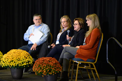 Four-person panel discussion on stage with yellow and orange mum flower arrangements