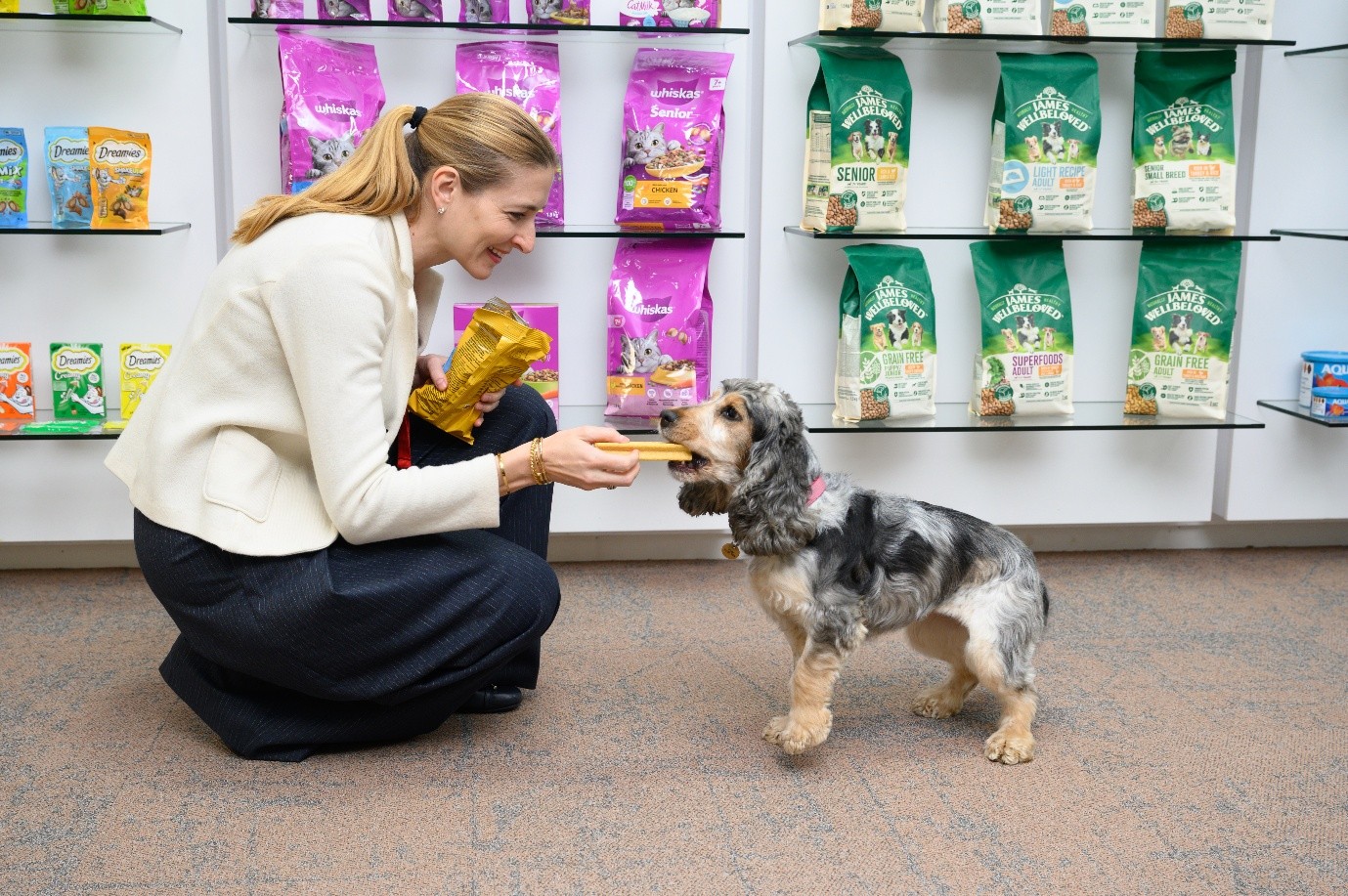 Woman offering dog treat to small terrier in pet food store with product shelves