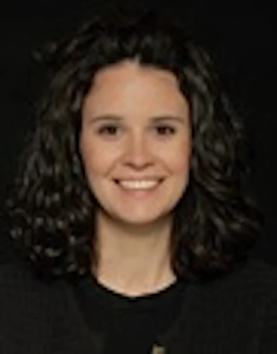 Professional headshot of a smiling woman with dark curly hair against a dark background