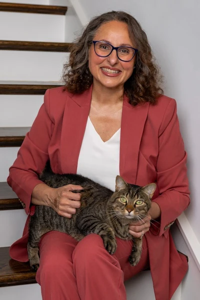 Professional woman in burgundy blazer holding tabby cat, smiling at camera