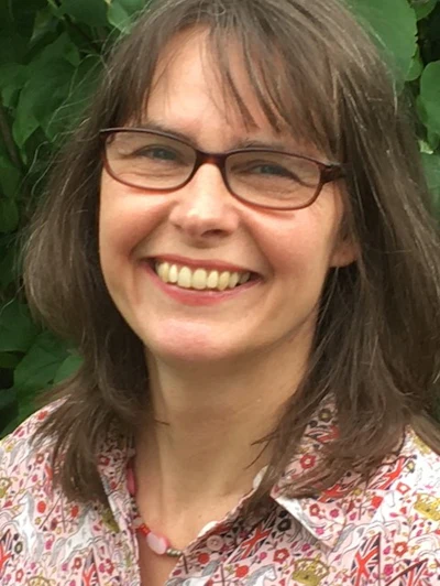 Woman with shoulder-length brown hair and glasses smiling outdoors wearing a colorful floral patterned shirt