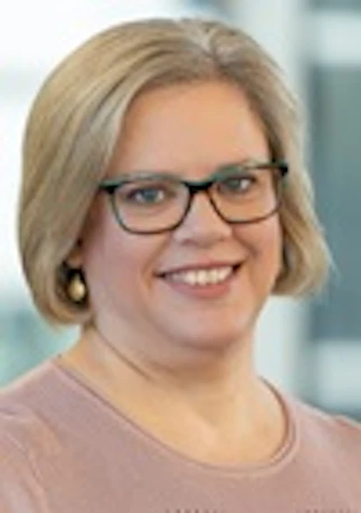 Professional headshot of a woman with blonde hair wearing glasses and a beige top