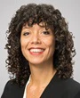 Professional headshot of a woman with curly dark hair wearing a black blazer and red lipstick