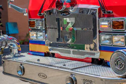 Close-up of red fire truck front grille with chrome details, blue and yellow striping, and headlights at station