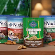 Nudges dog treats product lineup displayed on green football surface with football and accessories