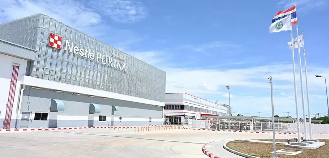 Nestlé Purina manufacturing facility with red checkered logo on white building facade and flags in foreground