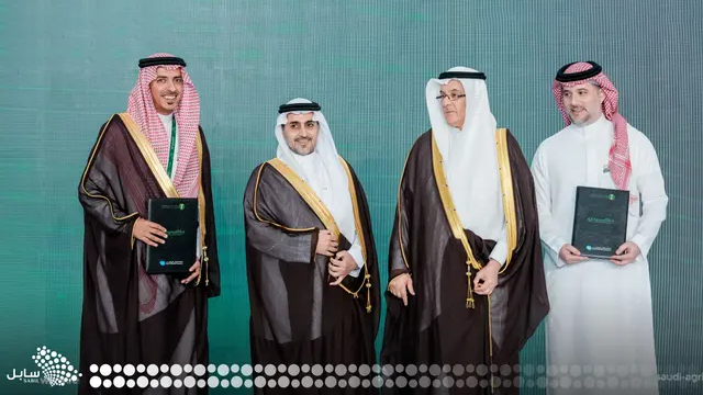 Four men in traditional Saudi Arabian formal attire posing together against a turquoise background