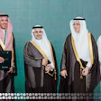 Four men in traditional Saudi Arabian formal attire posing together against a turquoise background