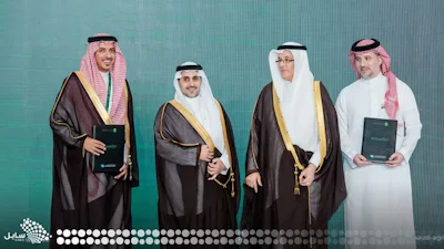 Four men in traditional Saudi Arabian formal attire posing together against a turquoise background