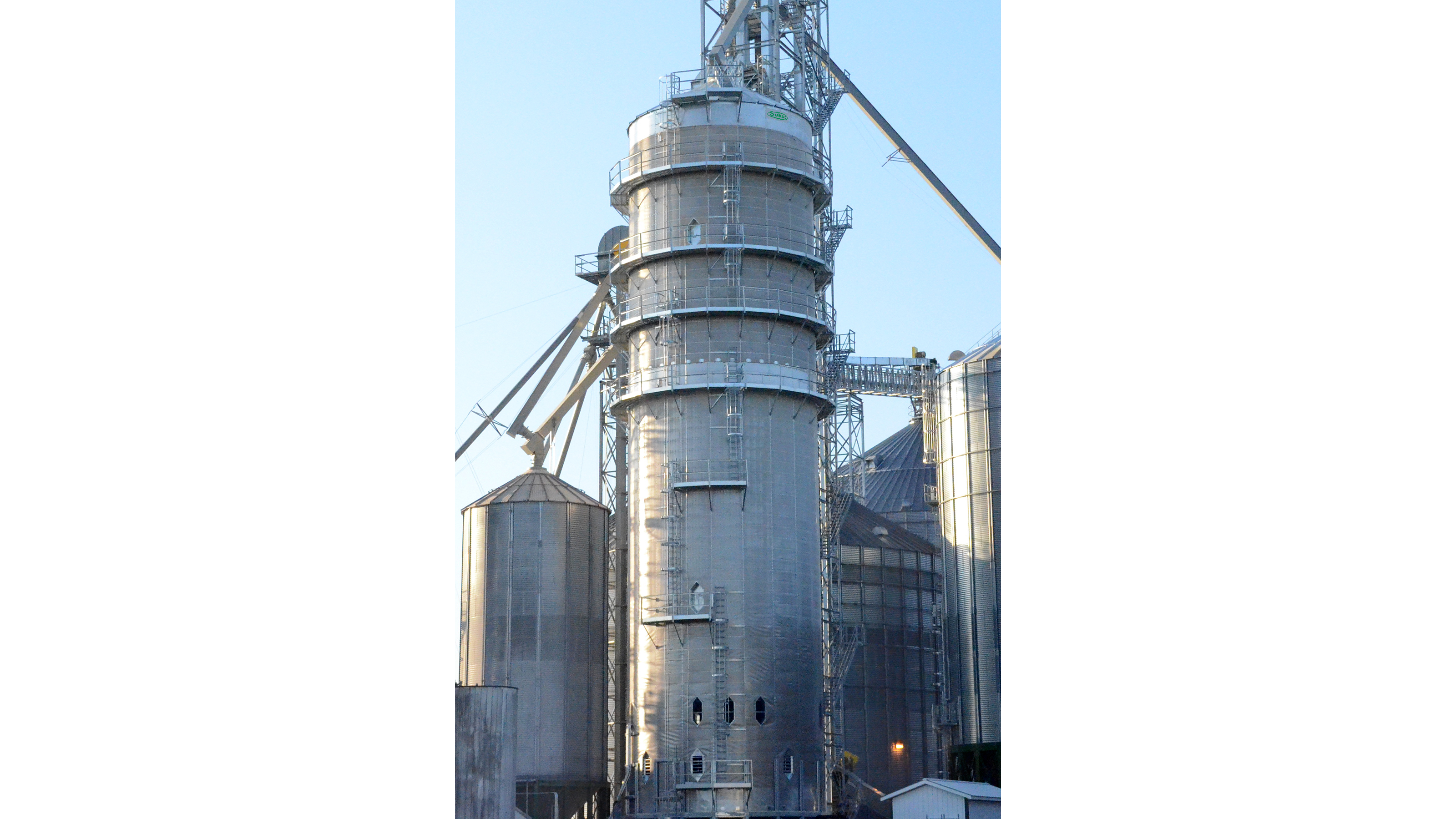 Industrial grain elevator with cylindrical metal silos and conveyor systems under clear blue sky