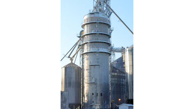 Industrial grain elevator with cylindrical metal silos and conveyor systems under clear blue sky
