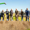 Group of seven business professionals holding shovels at a groundbreaking ceremony with green farm equipment and CHS signage