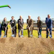 Group of seven business professionals holding shovels at a groundbreaking ceremony with green farm equipment and CHS signage