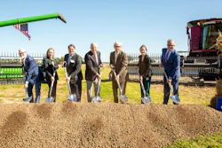 Group of seven business professionals holding shovels at a groundbreaking ceremony with green farm equipment and CHS signage