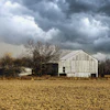 Weathered white barn in harvested field under dramatic storm clouds