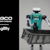 AGCO and Agility robotic agricultural robot with turquoise body holding black collection bin against gray background