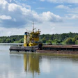 Yellow tugboat pushing a loaded barge on a river with forested banks under blue sky
