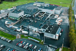 Aerial view of large industrial manufacturing facility with multiple buildings, parking lots, and surrounding green fields