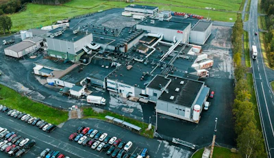 Aerial view of large industrial manufacturing facility with multiple buildings, parking lots, and surrounding green fields