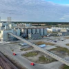 Large grain elevator facility with cylindrical storage silos, industrial buildings, and railroad tracks in rural landscape