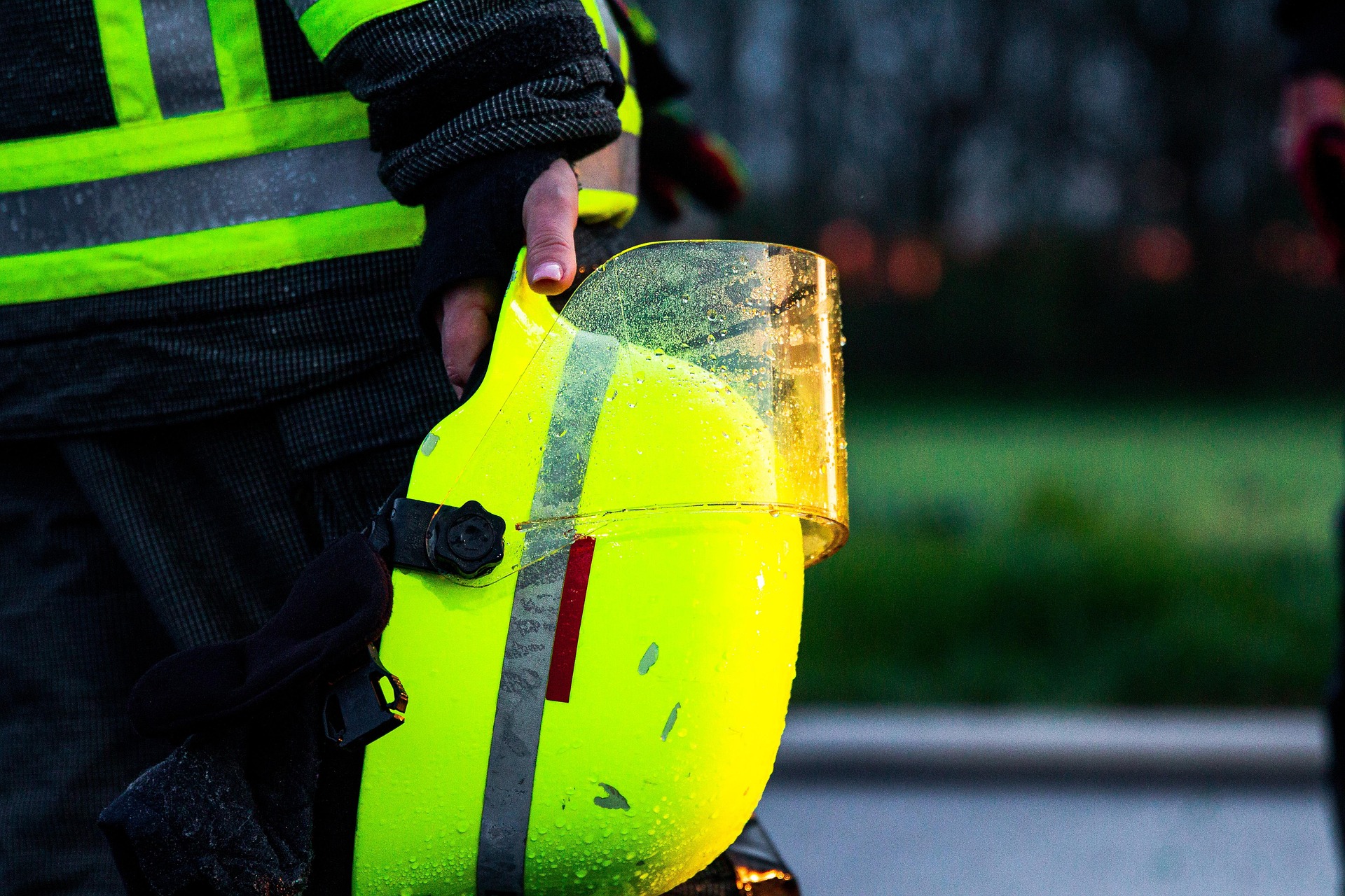 Worker in safety vest holding wet neon yellow hard hat with reflective stripes