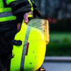 Worker in high-visibility vest holding a neon-yellow safety helmet with reflective stripes