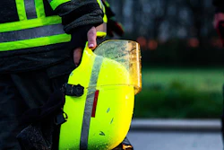 Worker in high-visibility vest holding a neon-yellow safety helmet with reflective stripes