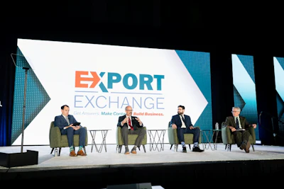 Four business professionals seated on stage during Export Exchange conference panel discussion with branded backdrop