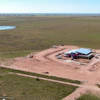 Aerial view of rural construction site with red barn and blue roof surrounded by green fields and dirt roads