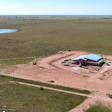 Aerial view of rural construction site with red barn and blue roof surrounded by green fields and dirt roads