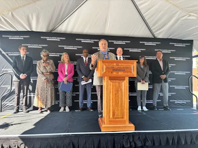 Southern Illinois University Edwardsville officials and guests at podium during formal outdoor event under tent