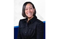 Professional headshot of a smiling woman wearing a black button-up shirt against a white background with blue accent