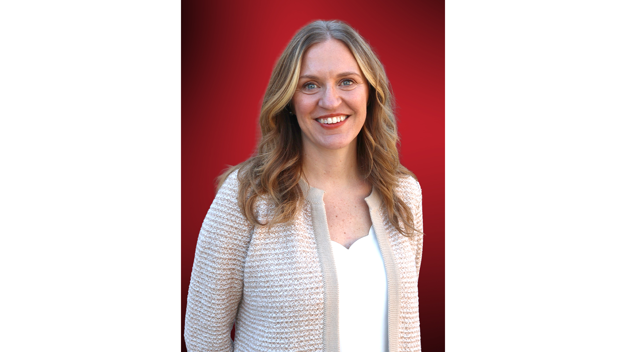 Professional headshot of a woman with wavy blonde hair wearing a cream cardigan over a white top, smiling against a red background