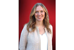 Professional headshot of a woman with wavy blonde hair wearing a cream cardigan over a white top, smiling against a red background